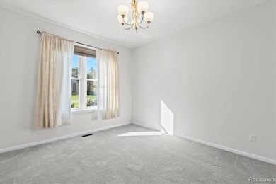 Carpeted spare room featuring a chandelier and baseboards