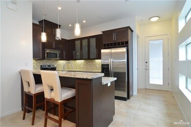 Kitchen with dark brown cabinetry, light stone countertops, appliances with stainless steel finishes, backsplash, and decorative light fixtures