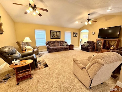 Carpeted living room with ceiling fan, vaulted ceiling, and arched walkways