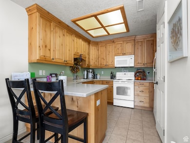 Kitchen featuring light countertops, white appliances, light tile patterned floors, a breakfast bar area, and a textured ceiling
