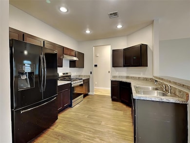 Kitchen featuring black refrigerator with ice dispenser, stainless steel gas range, a sink, under cabinet range hood, and light wood finished floors