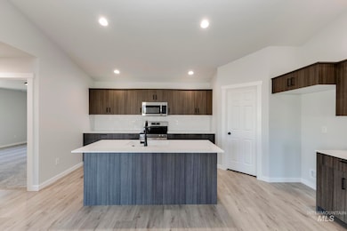 Kitchen featuring modern cabinets, a center island with sink, dark brown cabinets, recessed lighting, and stainless steel appliances