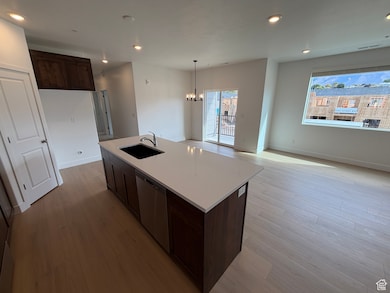 Kitchen featuring dark brown cabinetry, recessed lighting, light wood-style floors, pendant lighting, and light stone counters