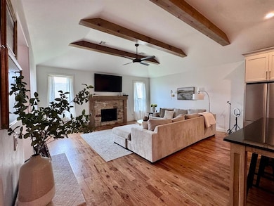 Living room featuring plenty of natural light, wood finished floors, a ceiling fan, and beamed ceiling