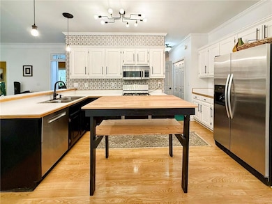 Kitchen featuring stainless steel appliances, white cabinets, a peninsula, ornamental molding, and light countertops