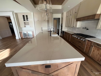 Kitchen with custom range hood, a large island, dark wood-style floors, decorative backsplash, and light stone counters