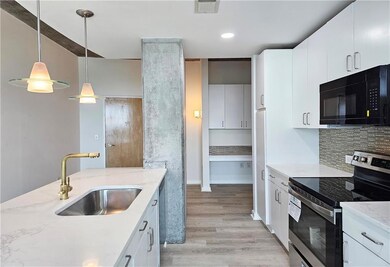 Kitchen with black microwave, stainless steel range with electric cooktop, a sink, light wood-style flooring, and light stone counters