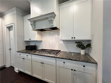 Kitchen with range hood, stainless steel gas cooktop, crown molding, decorative backsplash, and dark stone counters