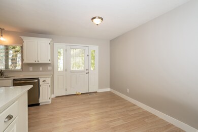 Kitchen with light wood finished floors, white cabinetry, stainless steel dishwasher, light stone countertops, and decorative light fixtures