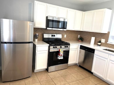 Kitchen featuring stainless steel appliances, white cabinetry, and tasteful backsplash