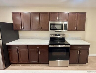 Kitchen featuring appliances with stainless steel finishes, dark brown cabinetry, light countertops, and light wood-style flooring