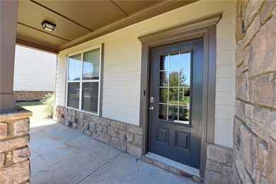 Entrance to property featuring generous covered porch with lighting and stone siding. Digital keypad on front door.