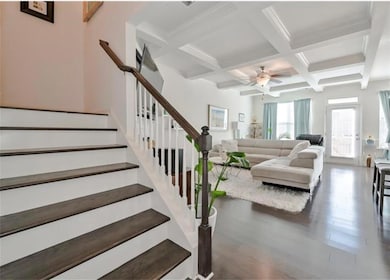 Staircase featuring beam ceiling, coffered ceiling, ceiling fan, and wood finished floors