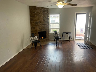 Sitting room featuring ceiling fan, dark wood-type flooring, a textured ceiling, a textured wall, and a stone fireplace