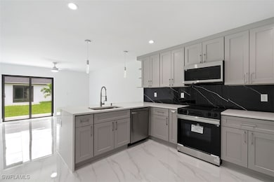 Kitchen featuring appliances with stainless steel finishes, a peninsula, backsplash, light marble finish floors, and gray cabinets