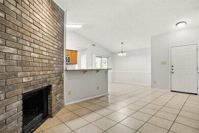 Unfurnished living room with lofted ceiling, light tile patterned floors, a brick fireplace, a chandelier, and a textured ceiling