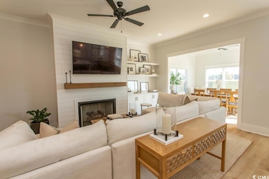Living area with a ceiling fan, light wood-style floors, recessed lighting, ornamental molding, and a fireplace