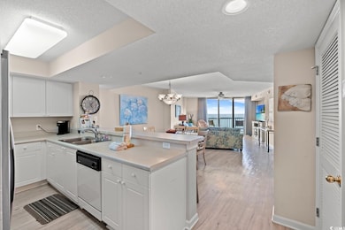 Kitchen featuring open floor plan, a textured ceiling, light countertops, white cabinetry, and a peninsula