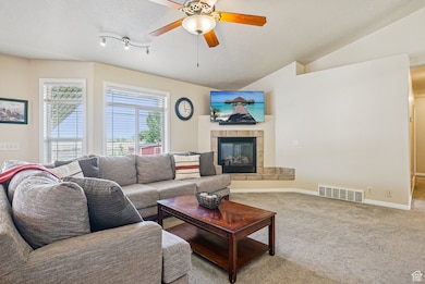 Living room featuring lofted ceiling, carpet flooring, a fireplace, a ceiling fan, and a textured ceiling