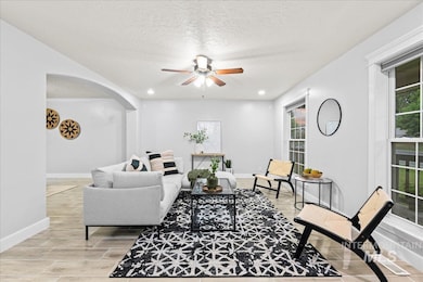 Living area featuring ceiling fan, a textured ceiling, plenty of natural light, arched walkways, and light wood finished floors