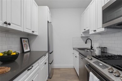Kitchen featuring decorative backsplash, stainless steel appliances, white cabinetry, light wood-style floors, and dark stone countertops