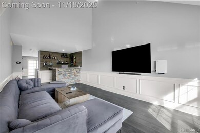 Living room with a wainscoted wall, a dry bar, a decorative wall, wood finished floors, and a high ceiling