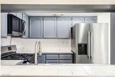 Kitchen featuring gray cabinetry, stainless steel fridge, and tile counters