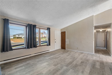 Unfurnished room featuring a baseboard heating unit, a textured ceiling, lofted ceiling, and light wood-style floors