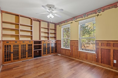 Empty room featuring light wood-style flooring, wainscoting, ceiling fan, built in features, and wood walls