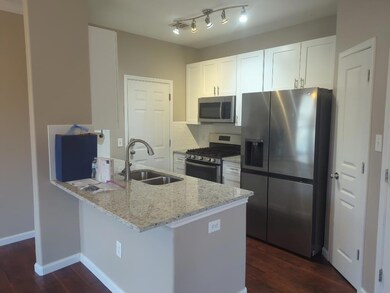 Kitchen with stainless steel appliances, light stone countertops, decorative backsplash, white cabinetry, and dark wood finished floors