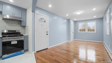 Kitchen featuring gas range, a baseboard heating unit, under cabinet range hood, decorative backsplash, and recessed lighting
