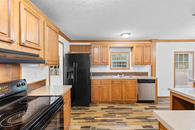 Kitchen featuring black appliances, wood finished floors, a sink, light countertops, and under cabinet range hood
