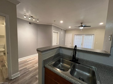 Kitchen with a sink, crown molding, a ceiling fan, dark countertops, and wood finished floors