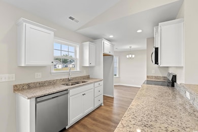 Kitchen with light stone counters, appliances with stainless steel finishes, white cabinets, recessed lighting, and vaulted ceiling