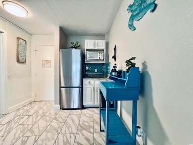 Kitchen featuring white cabinetry, freestanding refrigerator, backsplash, light marble finish floors, and a textured ceiling