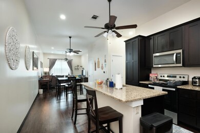 Kitchen featuring appliances with stainless steel finishes, light stone counters, dark wood-type flooring, a breakfast bar, and an island with sink