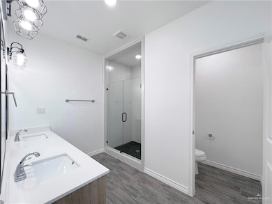 Bathroom with wood finished floors, toilet, a stall shower, and baseboards