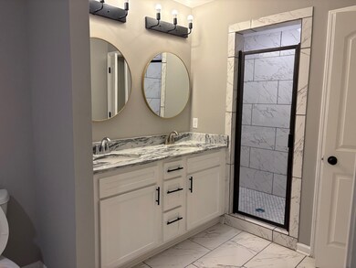 Full bathroom featuring marble finish flooring, double vanity, and a stall shower