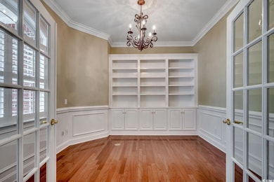 Unfurnished dining area with crown molding, light wood-type flooring, a chandelier, a decorative wall, and a wainscoted wall
