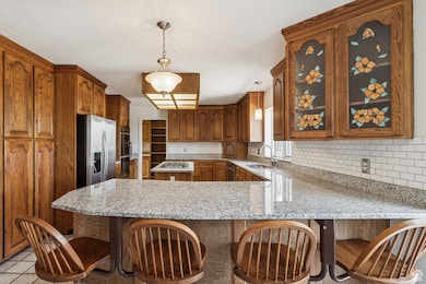 Kitchen with light stone counters, a kitchen breakfast bar, a peninsula, and pendant lighting