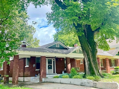 View of front of house featuring a chimney, brick siding, a shingled roof, and covered porch