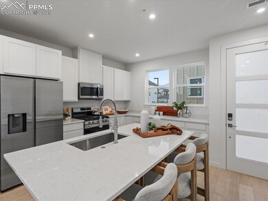 Kitchen featuring stainless steel appliances, a kitchen breakfast bar, light stone counters, white cabinetry, and light wood-style floors