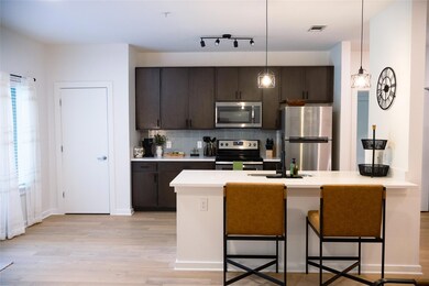 Kitchen featuring dark brown cabinets, a kitchen breakfast bar, stainless steel appliances, hanging light fixtures, and tasteful backsplash