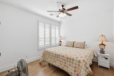 Bedroom with wood like floors, ceiling fan and plantation shutters.