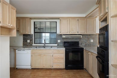 Kitchen with backsplash, sink, extractor fan, light stone counters, and black appliances