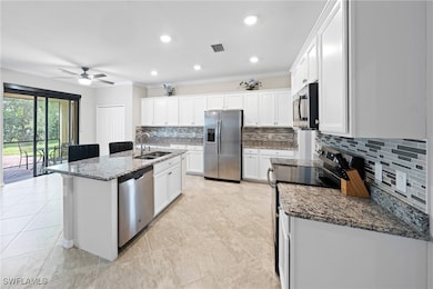 Kitchen featuring appliances with stainless steel finishes, decorative backsplash, dark stone countertops, white cabinets, and a kitchen island with sink
