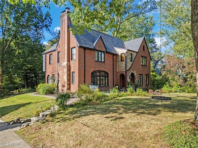 Tudor-style house featuring a front lawn, a chimney, brick siding, and view of wooded area