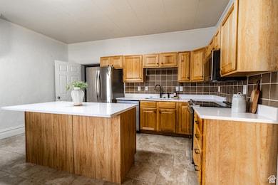 Kitchen with backsplash, a kitchen island, brown cabinetry, stainless steel appliances, and ornamental molding
