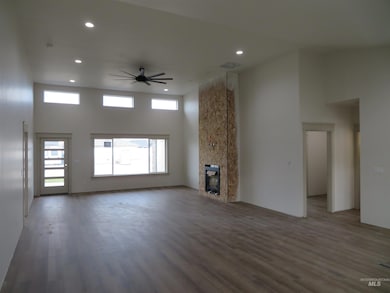 Unfurnished living room featuring a towering ceiling, a ceiling fan, wood finished floors, a large fireplace, and recessed lighting