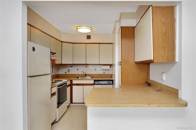 Kitchen with white appliances, under cabinet range hood, a peninsula, light countertops, and cream cabinetry